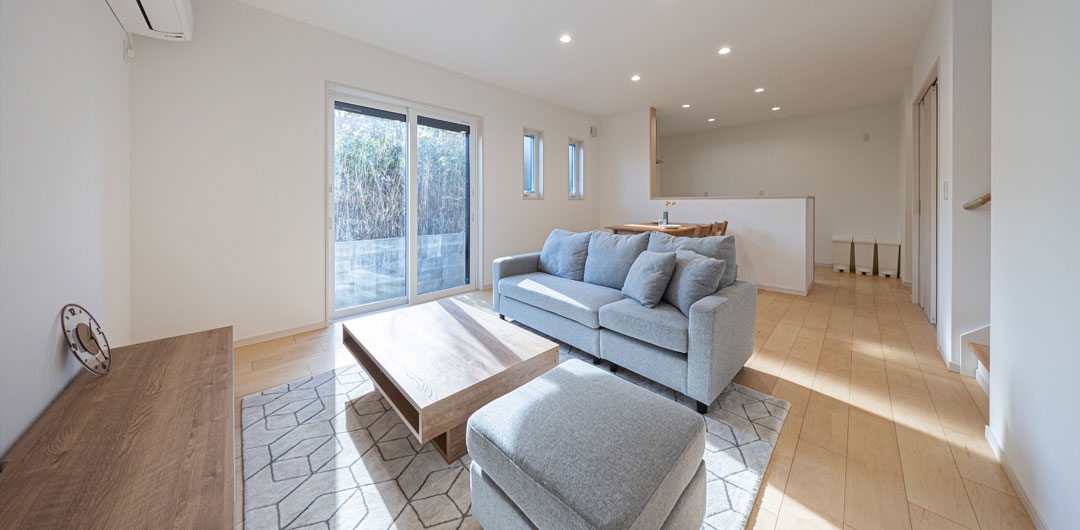 木目のフローリングとグレーのソファを配置したリビング。掃き出し窓から自然光が入る空間。